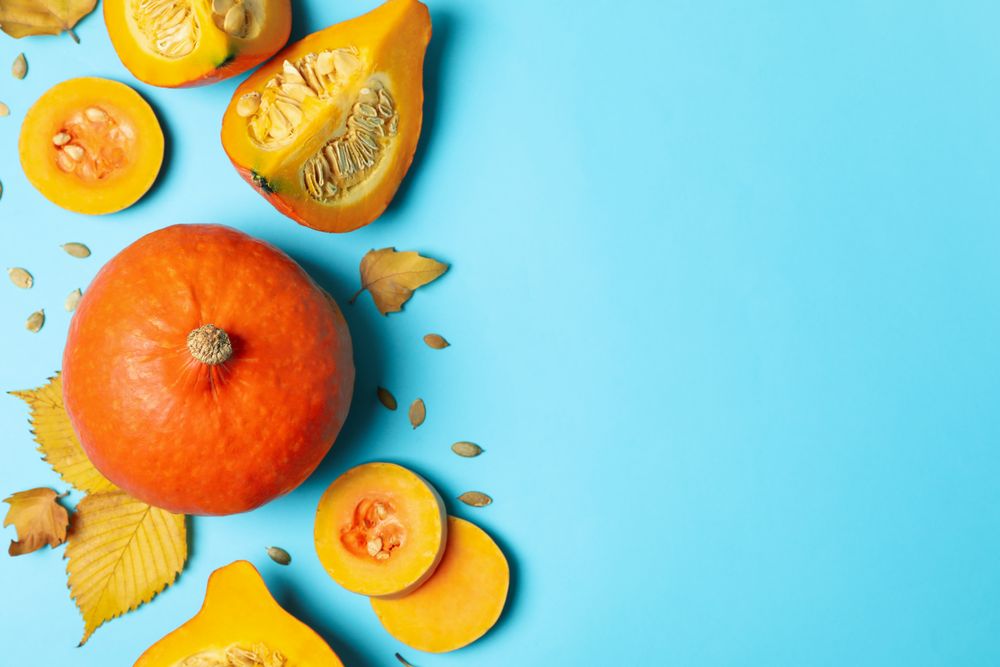 Composition with pumpkin, slices, leaves and seeds on blue background