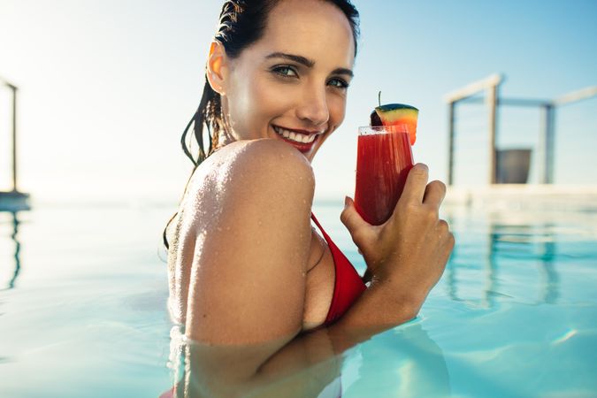 Beautiful female in bikini having a drink in pool on summer day