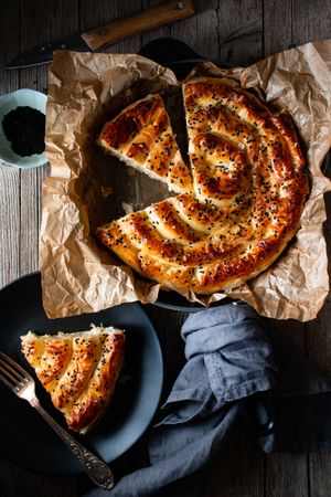 From above crop cook holding hot baking dish with fresh puff pastry and serving piece of borek on plate