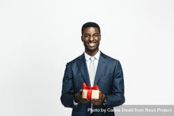 Smiling Black man presenting present wrapped in gold paper with red bow 5nx28b