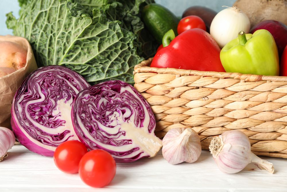 Wicker basket and vegetables on wooden background, close up
