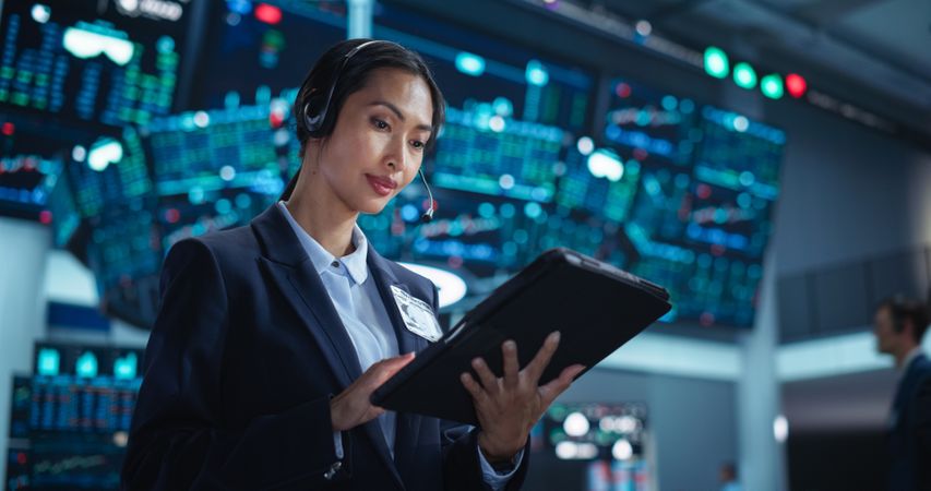 Young Asian Female Broker Working on Tablet Computer on Stock Exchange Floor.