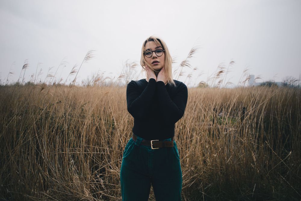 Young attractive blonde female model with glasses posing in wheat field on cloudy day