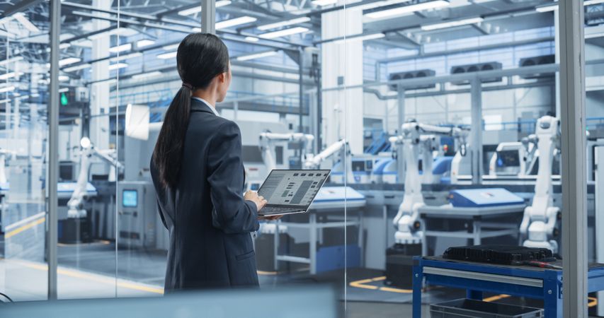 Electronics Manufacturing Technician Working on a Laptop Computer at a Factory Space. Asian Female Specialist Developing, Maintaining, Fine-Tuning Programs for Machine Production and Assembly