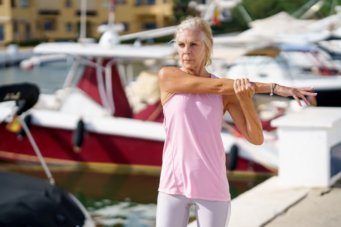 Older female in pink athletic wear stretching her arms before workout