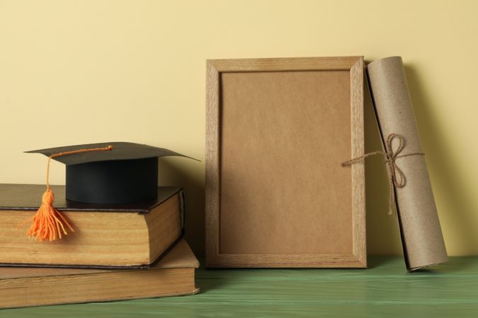 Frame and graduate hat with books on table.