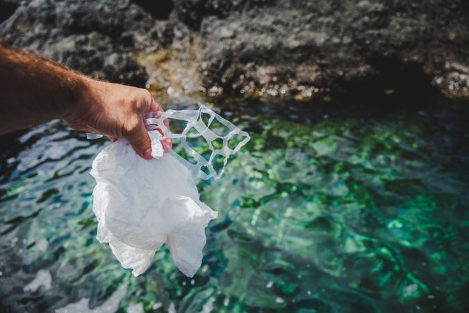 Crop man pulling plastic bag out of water