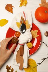 Spoon in towel on plate, leaves and hand on blank background, top view