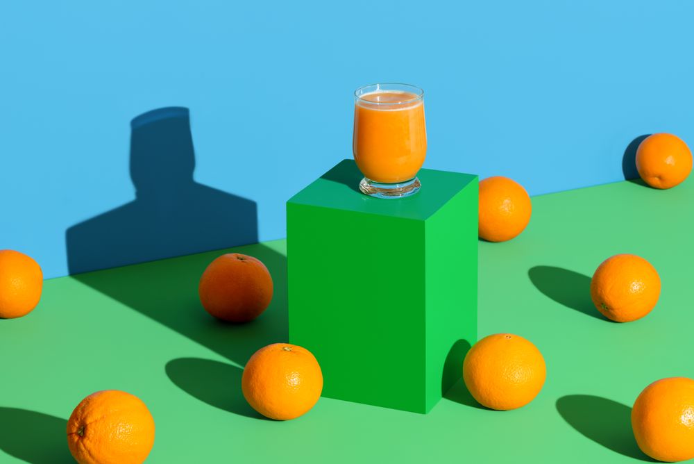 Orange juice glass on a stand in bright light on a vibrant colored background
