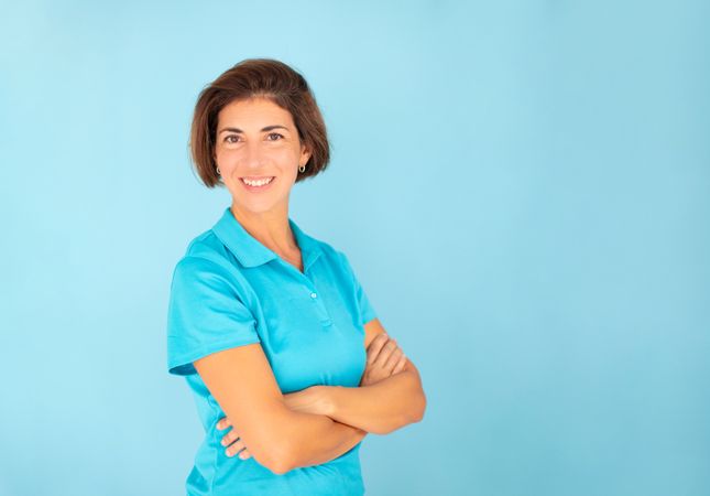 A woman, a physiotherapist, poses with a confident gesture, looking at the camera on a blue background, wearing a blue T-shirt