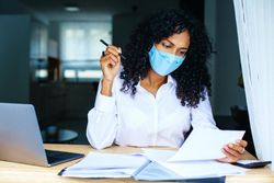 Woman reading over documents with a laptop while wearing a facemask