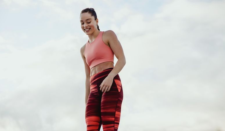 Muscular female smiling in workout clothing against sky