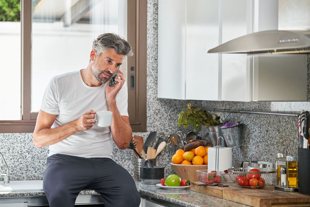 Man talking on cellphone and drinking coffee in kitc