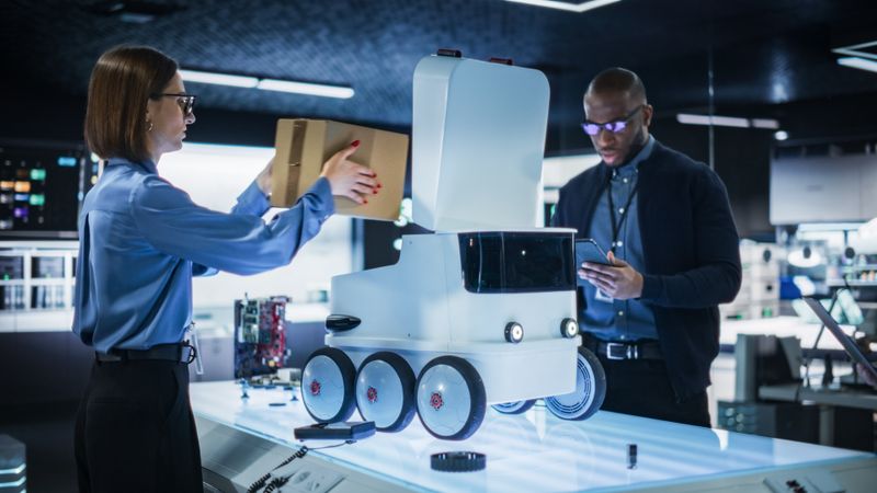 Diverse Team of Industrial Specialists Working on Remotely Controlled Mobility Robot in a Research Facility. Engineer Testing the Parcel Compartment of the Delivery Machine with Self-Driving Autopilot