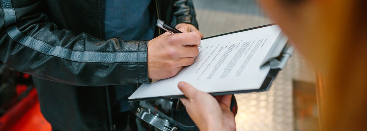 Biker man signing insurance policy on workshop while female mechanic holding clipboard