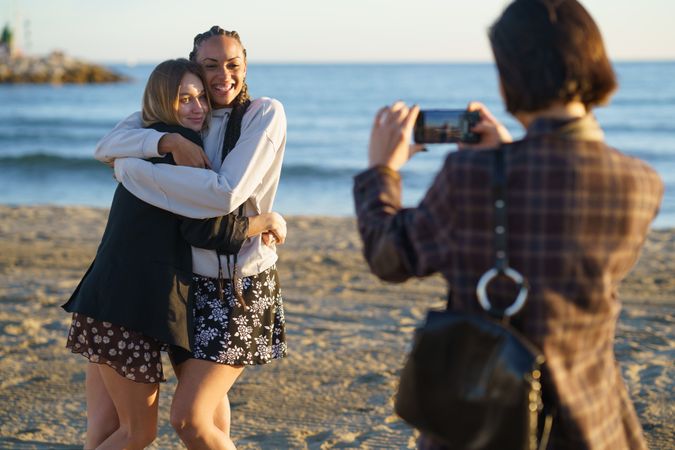 Happy girlfriends having fun and taking pictures of each other on beach at sunset