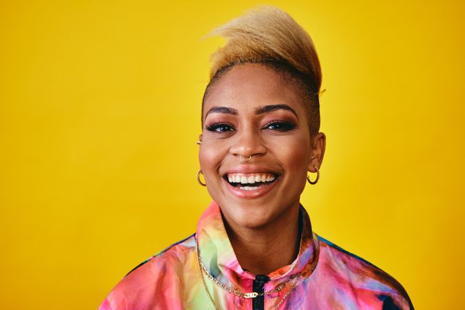 Studio shot of smiling Black woman in colorful 80s windbreaker jacket and gold jewelry