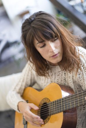 Female in wool sweater strumming acoustic guitar