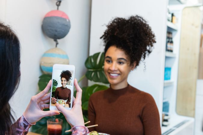 Crop woman taking photo of friend in restaurant