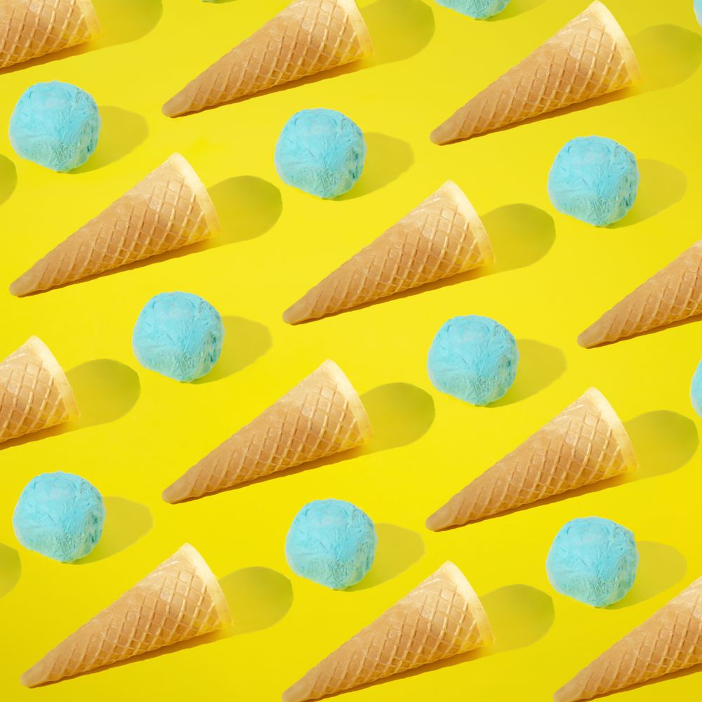 Rows of blue ice cream scoops and cones on yellow background