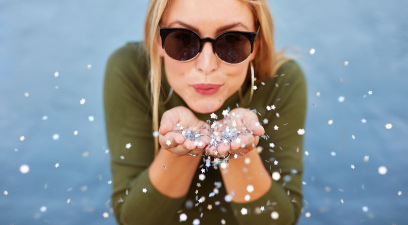 Close up portrait of blonde young woman blowing glitters