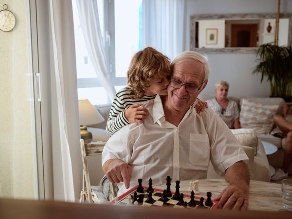 Tender grandson hugging grandfather playing chess game
