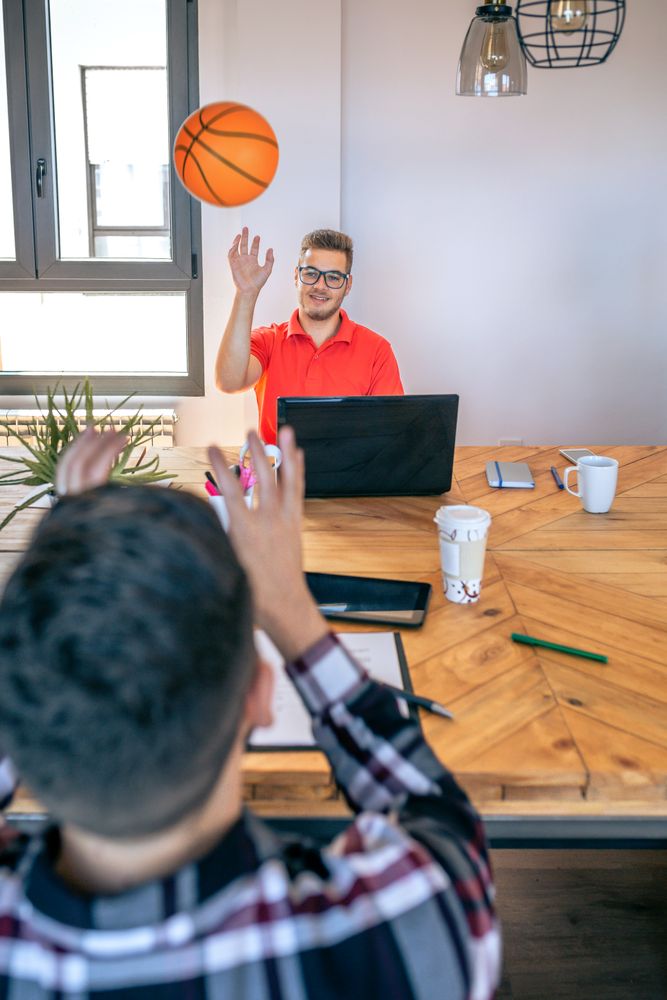 Businessman in brainstorm having fun throwing a basket ball to colleague in office