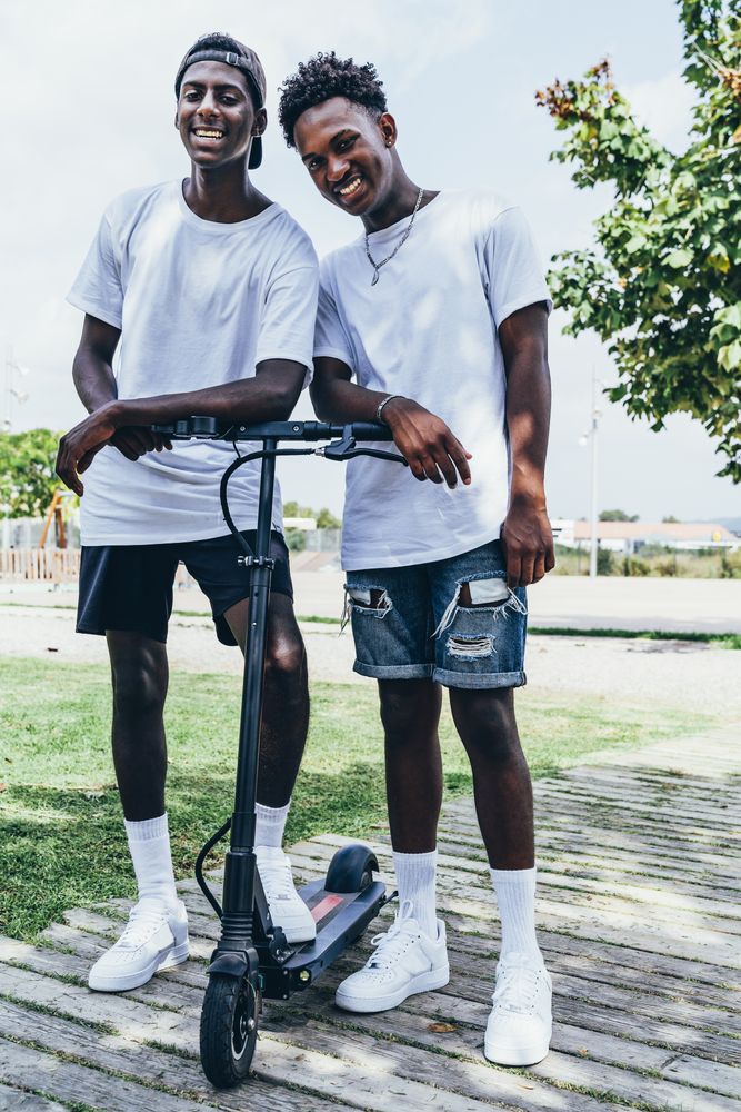 Black man riding on electric scooter in park with friend on back