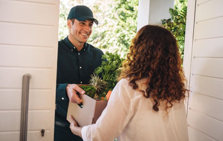 Delivery man hands over box of groceries at the house door