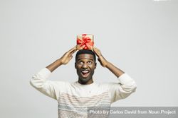 Excited Black man holding gold box with red bow above his head 56nLl5