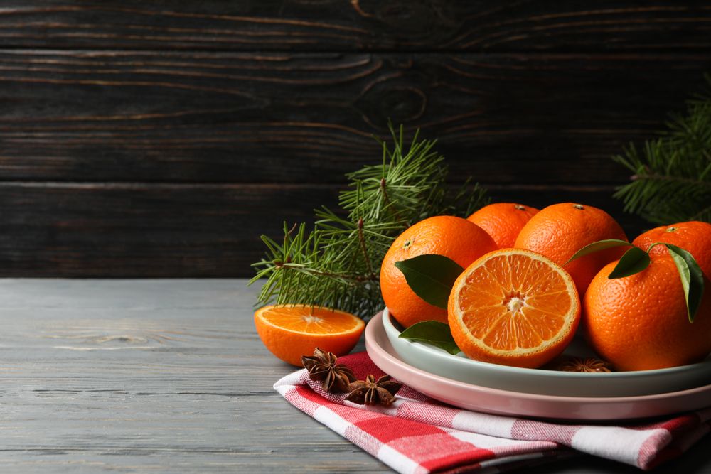 Plates with mandarins, pine branches, napkin and cinnamon on wooden background