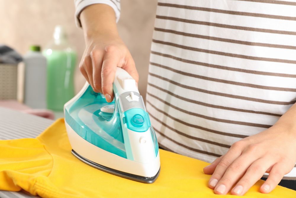 Young woman ironing yellow t-shirt, space for text