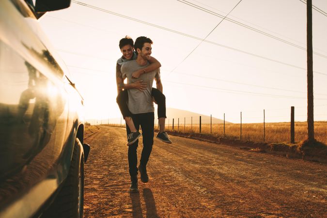 Cheerful male carrying woman on his back on dirt road