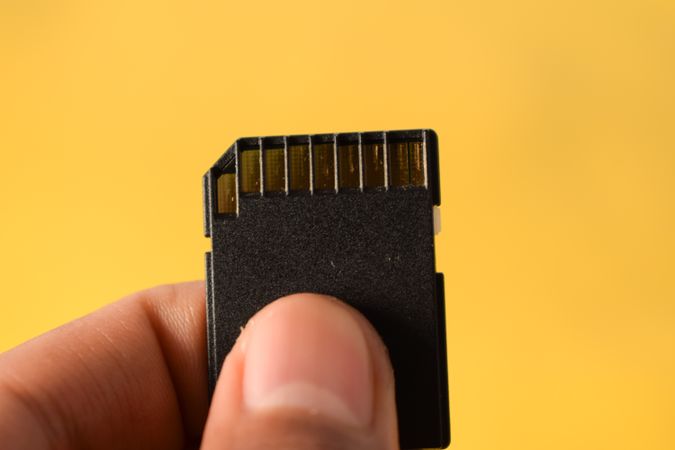 Close up of SD card in hand with yellow background