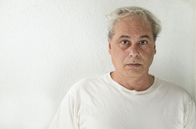 Portrait of surprised middle aged man in light shirt against light wall