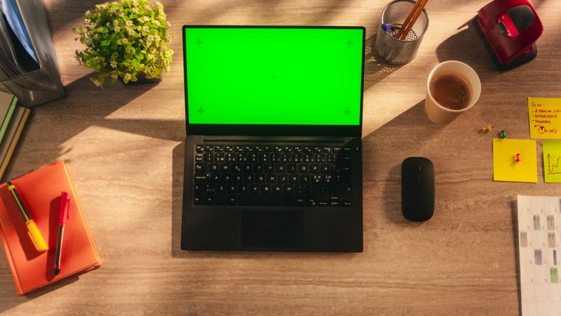 Laptop Computer On the Home Office Table with Mock Up Green Screen Chromakey Display with Motion Tracker Placeholders. Top Down View Of Workplace Of An Employee With Pans, Notebooks And Calendar