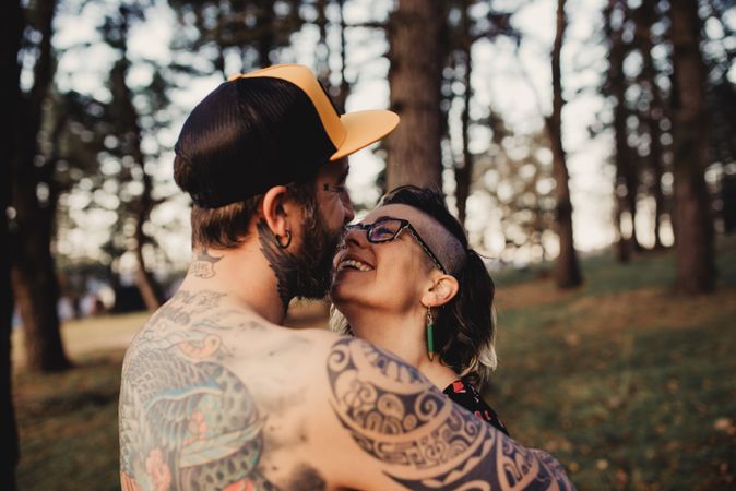 Young guy in tattoos hugging woman in forest