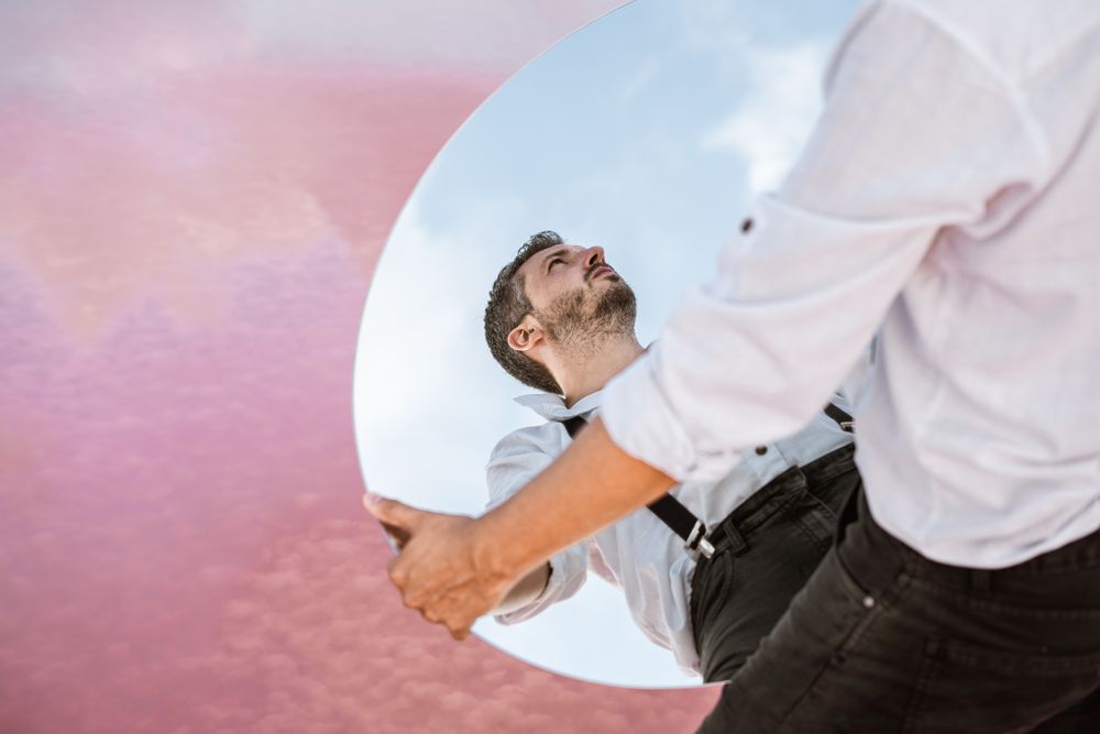 Stylish man holding mirror with reflection