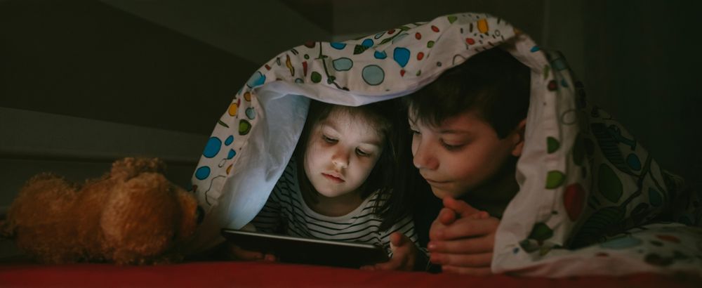 Siblings looking at the tablet in the dark