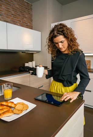 Woman checking tablet while having breakfast at home before work, vertical composition