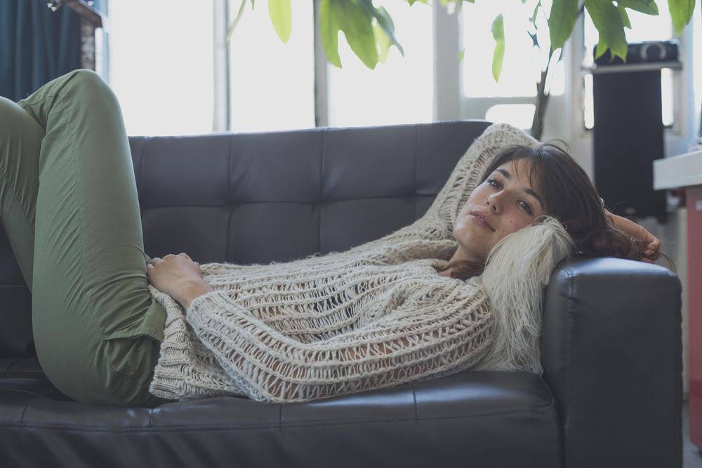 Female in wooly sweater relaxing on leather couch in living room