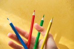 A child's hand picking up coloured pencils on a yellow backgroun
