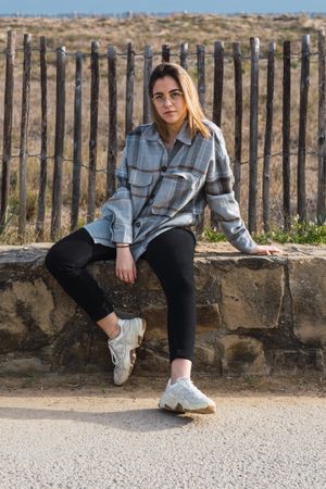 Trendy young female millennial resting on stone border at roadside