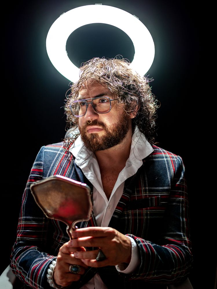 Serious man with glowing fake nimbus holding mirror and looking away