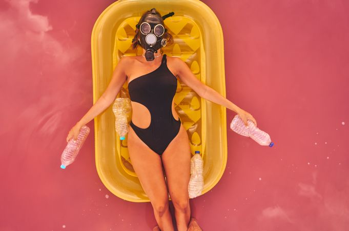 Female in gas mask and with plastic bottles in lake water