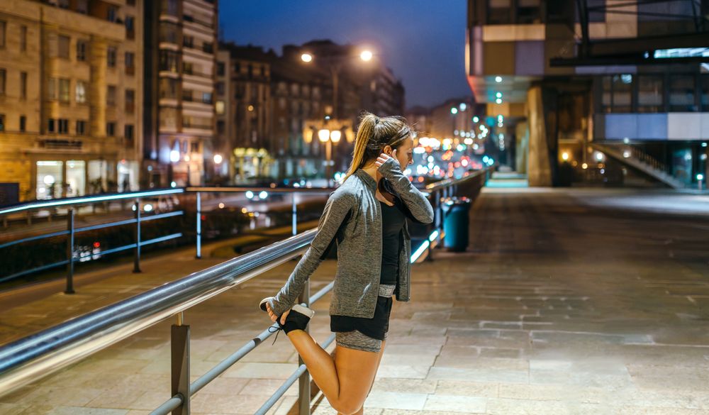 Female runner stretching her legs before training at night in town
