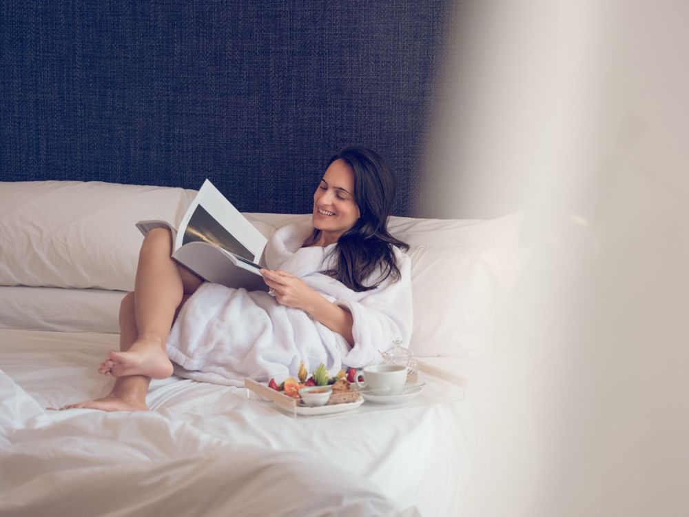 Smiling woman reading magazine during breakfast on bed