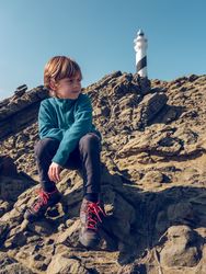 Boy sitting on rocks against lighthouse