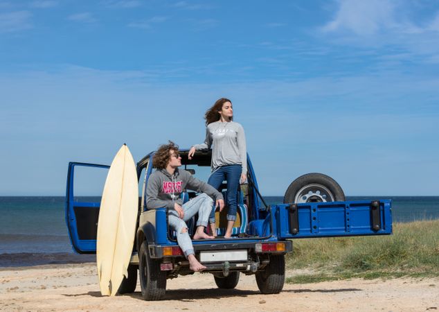 Guy with surfboard and woman on roof of car