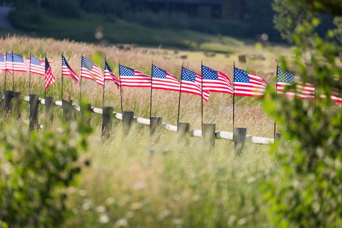 Row of American Flags  Waving in the Wind Along A Fence.
